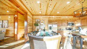 Interior de una cabaña de madera con cocina, que incluye armarios de madera, una isla central con taburetes y una mesa de comedor.