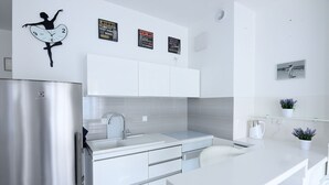 A modern kitchen with a stainless steel refrigerator, white cabinets, a sink, and a decorative wall clock. - Victus Apartamenty - Cadena 3 (Sopot)