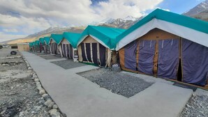 A row of numbered tents with a concrete pathway in a mountainous area. - TIH P3 Camp - Pangong (Leh)