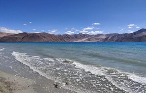 A beach with clear water and distant mountains. - TIH P3 Camp - Pangong (Leh)