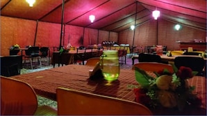 A tented dining area with tables and chairs, a pitcher of water, and a vase with flowers. - TIH P3 Camp - Pangong (Leh)