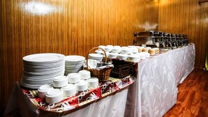 A buffet setup with stacked plates, bowls, and a variety of food items on a table covered with a patterned tablecloth.