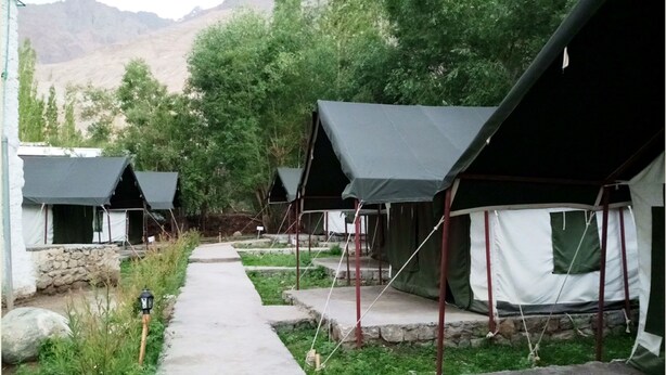 A row of tents with a concrete pathway between them, set in a natural landscape with mountains in the background.