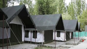A row of tents with a simple, functional design, set up on a concrete base with a pathway in front.