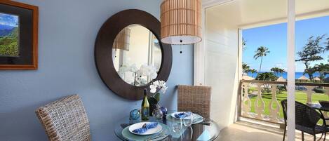A dining area with a glass table, wicker chairs, a mirror, and a view of the ocean.