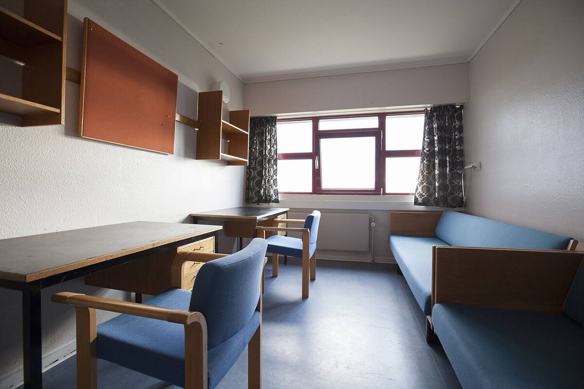 Ein Zimmer mit Schreibtisch, zwei Stühlen, einer Couch und einem Fenster mit Vorhängen.
