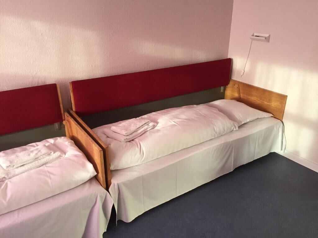 Una stanza con due letti singoli, ognuno dotato di una testata in legno e un pavimento scuro.