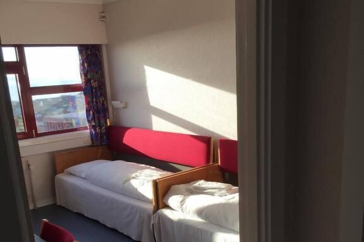 Ein kleines, kompaktes Zimmer mit zwei Einzelbetten, einem kleinen Tisch und einem Stuhl.