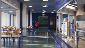 Een biljartzaal met tafels, stoelen, een pooltafel en een bar met een koffiemachine.