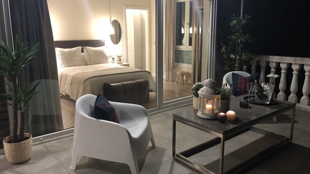 Una camera da letto moderna con un letto grande, una porta vetrata che dà su un balcone e un tavolino con candele e una bottiglia.