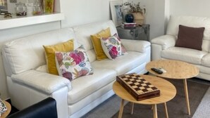Un soggiorno moderno con un divano bianco, un tavolino da caffè e una poltrona nera. Ci sono cuscini decorativi e un quadro incorniciato sul divano.