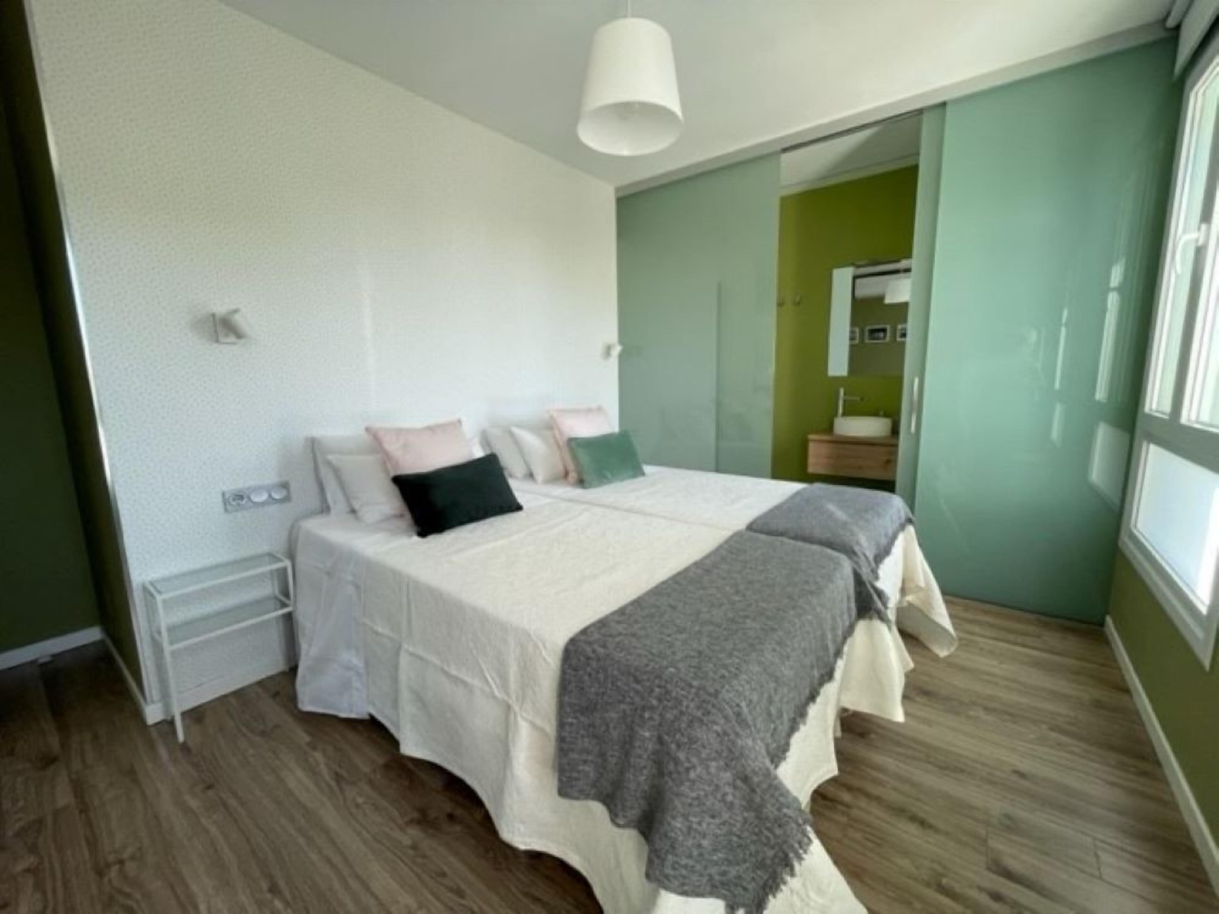 A bedroom with a bed, bedside tables, a mirror, and a window.