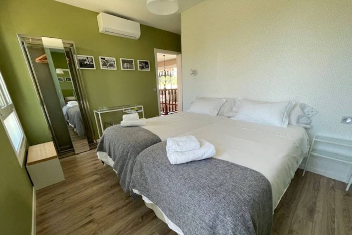 A bedroom with two beds, a mirror, a radiator, and a door leading to a balcony.
