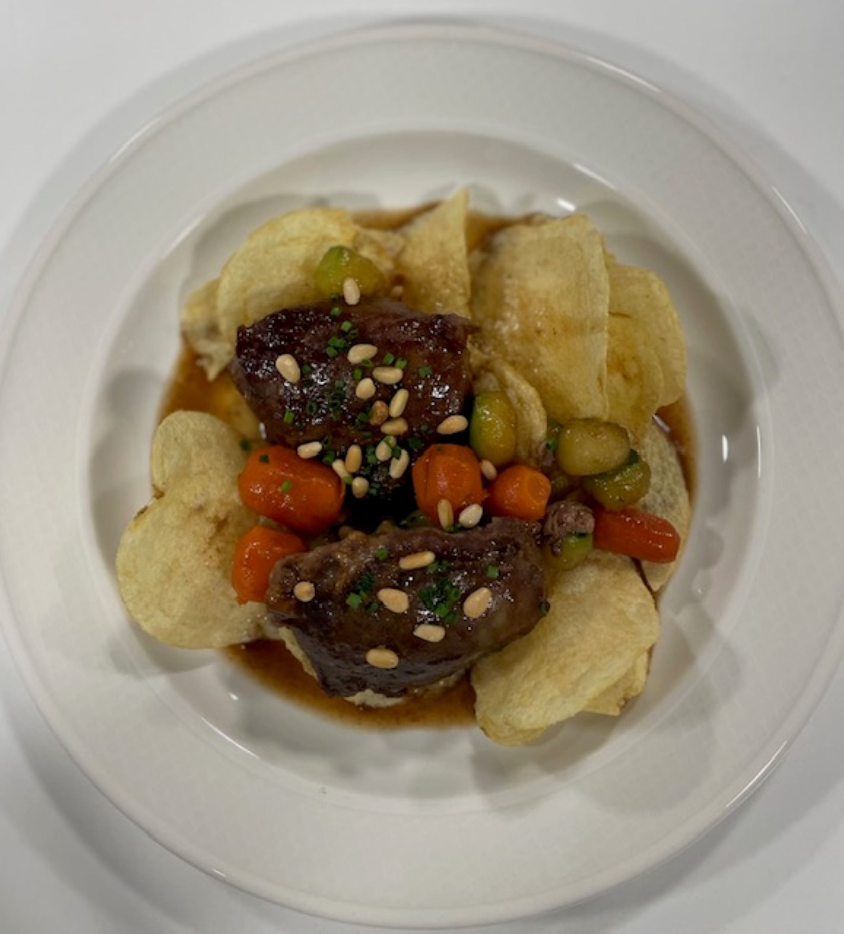 A plate with a beef dish, vegetables, and chips.