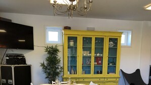 Zona pranzo con un lungo tavolo apparecchiato per sei persone, sedie bianche, un armadietto giallo con vetri e un lampadario.