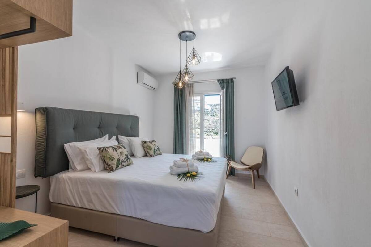A modern bedroom with a large bed, a TV mounted on the wall, and a view of the outdoors through the window.