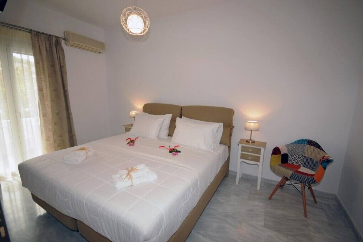 A neatly made bed with white linens and decorative pillows, a bedside table with a lamp, and a colorful chair.