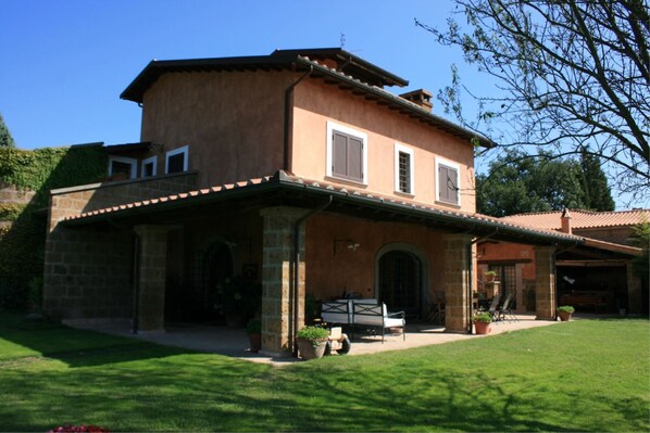 A two-story house with a stone facade, a covered patio, and a lawn. - Villa Iris (Corchiano)