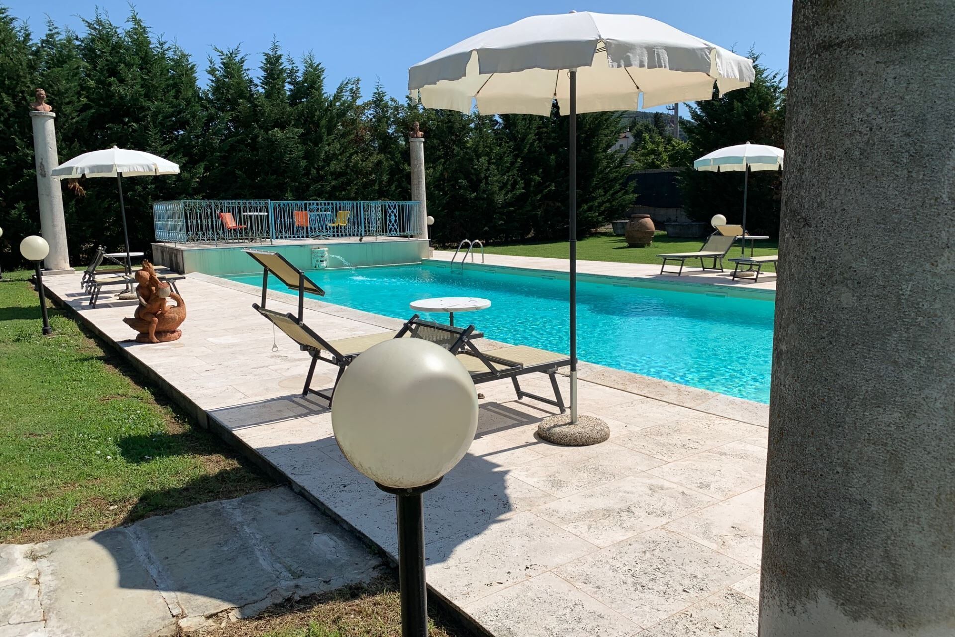 A swimming pool area with lounge chairs, umbrellas, and a statue.