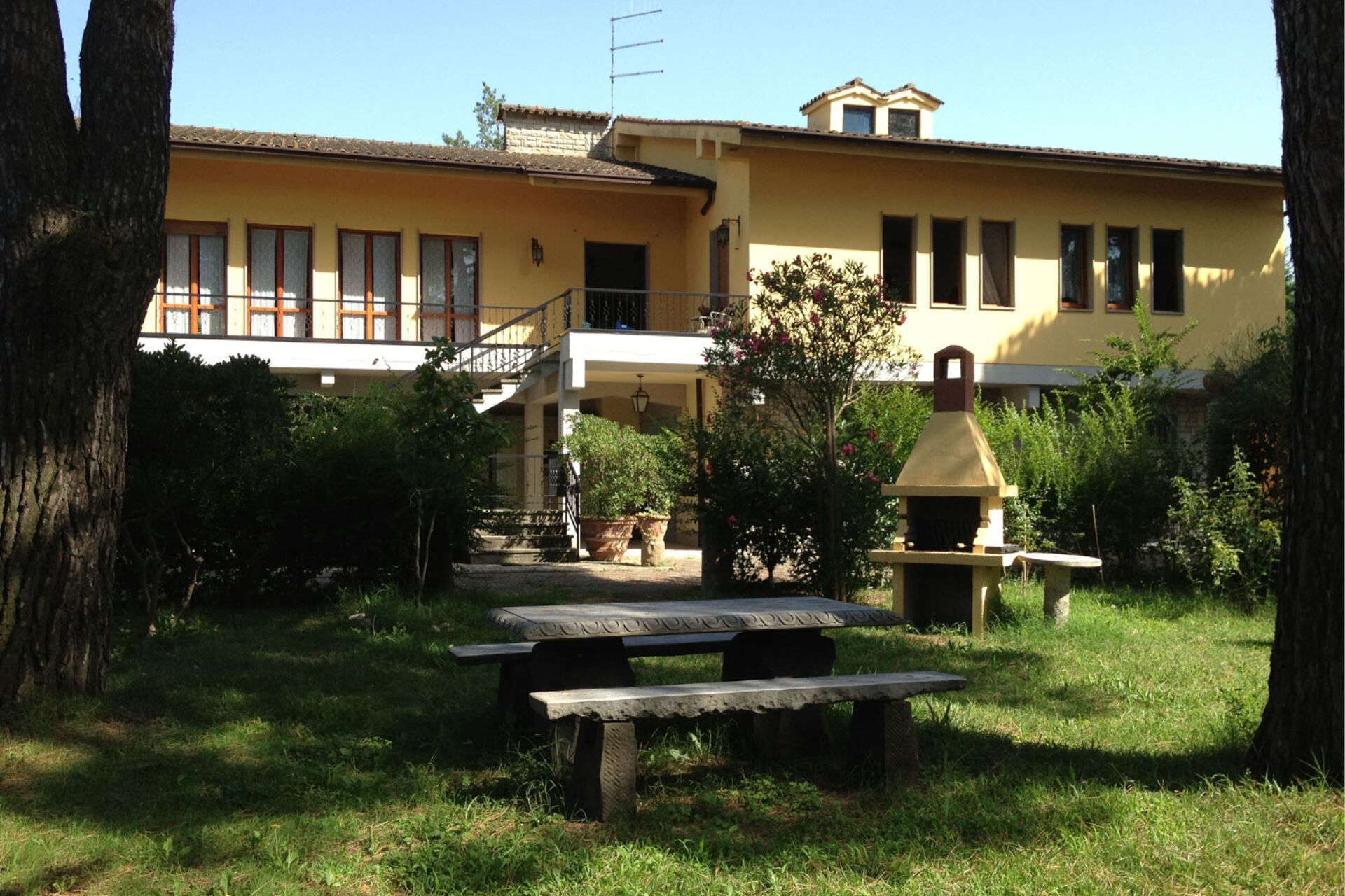 A two-story building with a balcony, a barbecue grill, and a picnic table in the yard.