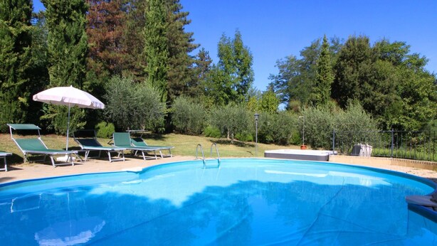 A swimming pool with green lounge chairs and a white umbrella. - Villino Alba (Arezzo)