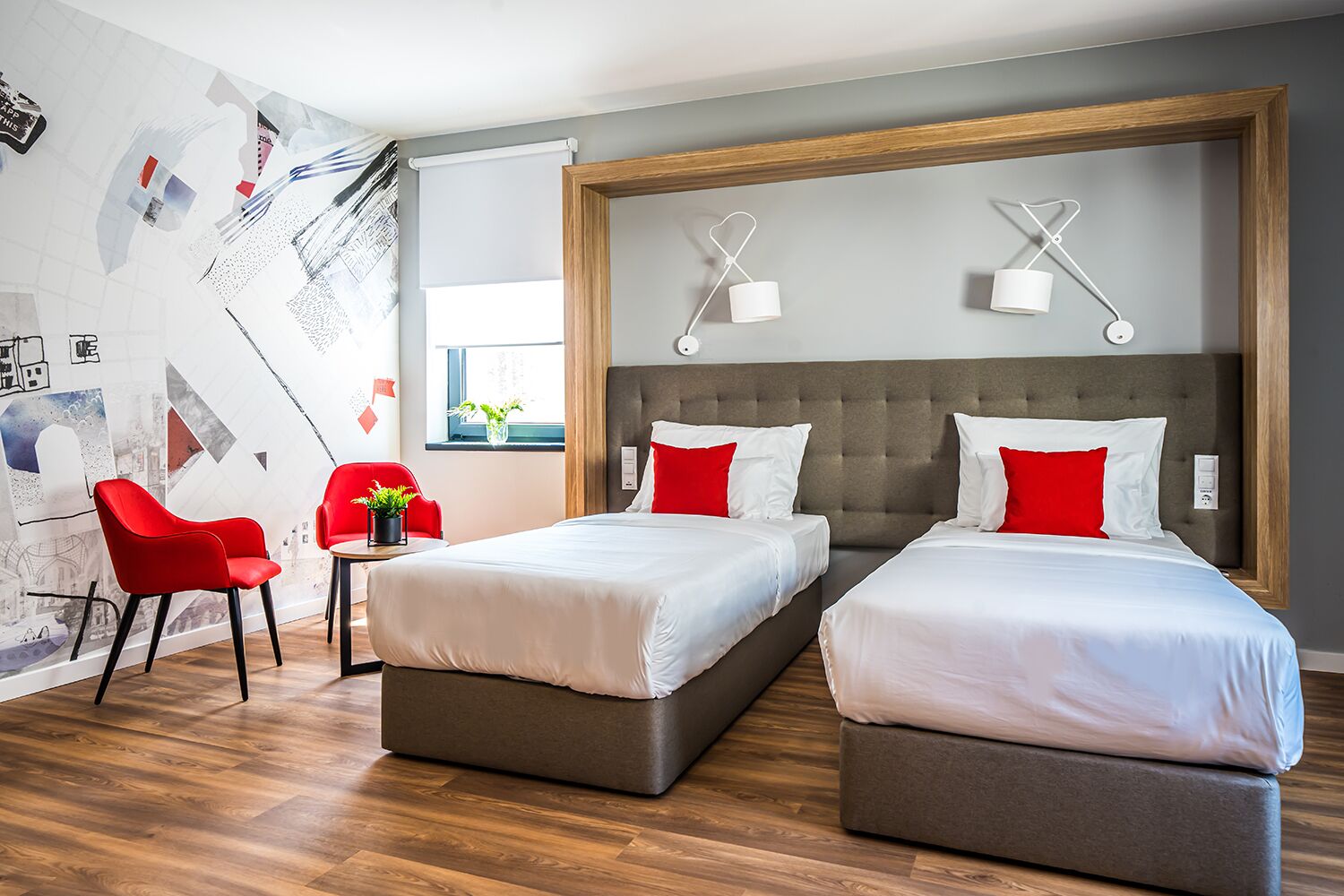 A hotel room with two beds, a red chair, a small table with a plant, and a wall with abstract art.