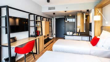 A modern hotel room with two beds, a desk with a red chair, a TV, and a large mirror.