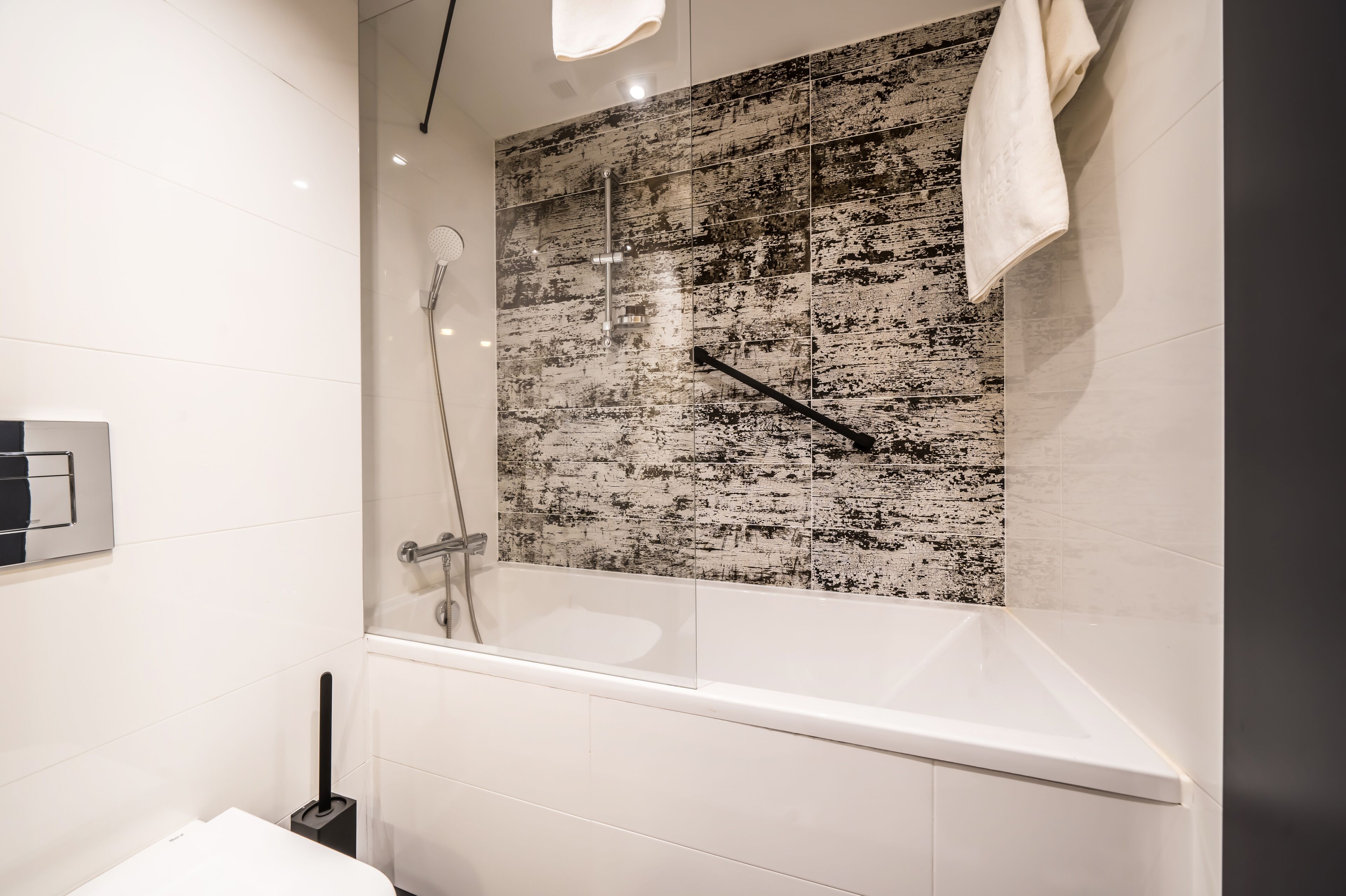 Ein modernes Badezimmer mit einer Glaskabine zur Dusche, weißen Fliesen und einer strukturierten Wand.