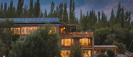 Un edificio moderno de varios pisos con amplios ventanales y paneles solares, rodeado de un bosque denso y montañas.