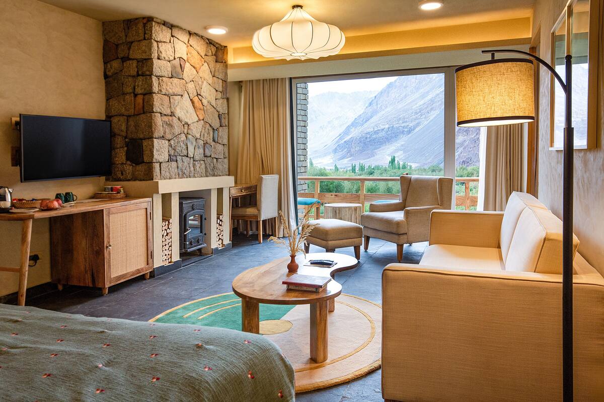 A hotel room with a stone fireplace, a television, a sofa, and a view of mountains.