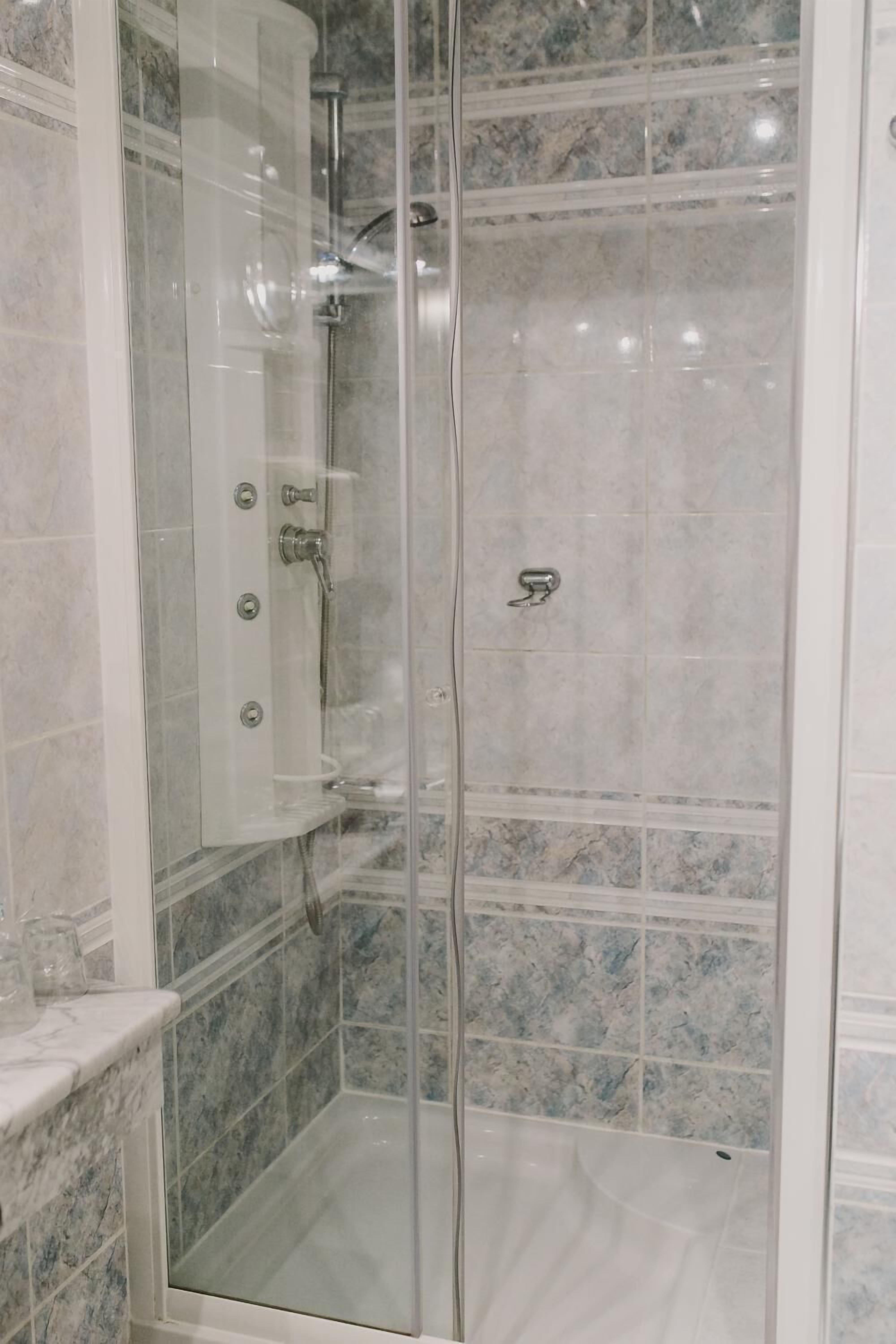 Una ducha con cerramiento de vidrio y pared revestida de mármol.