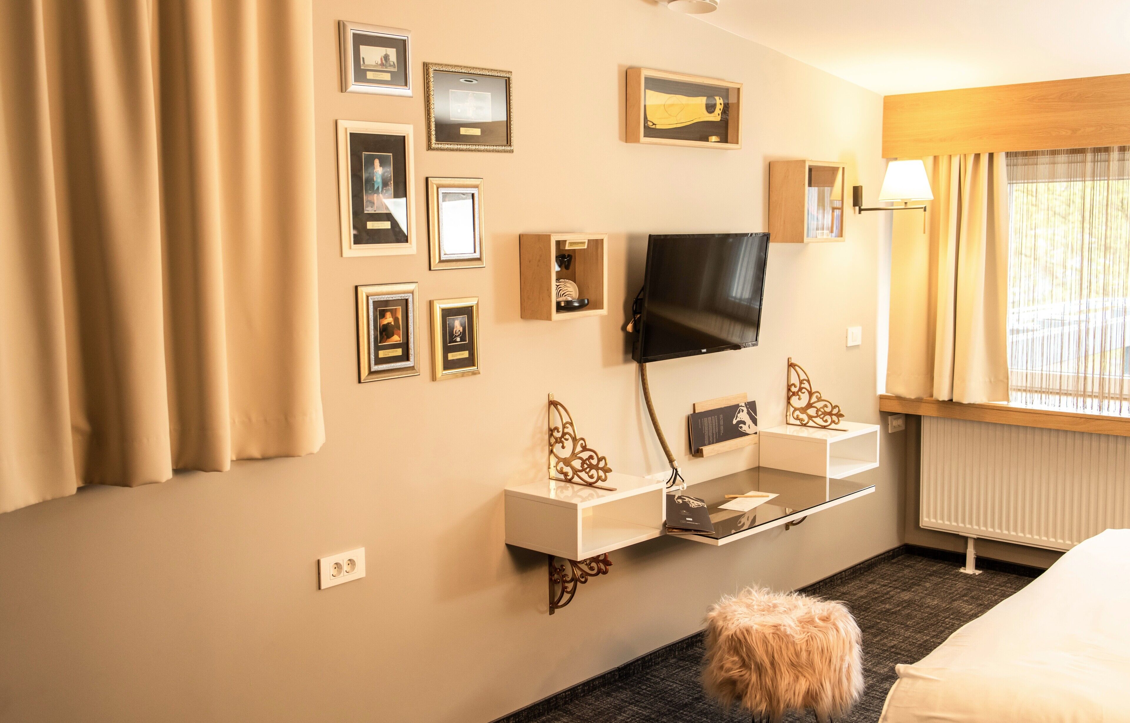 A hotel room with a bed, a TV mounted on the wall, a small table, and a window with curtains.