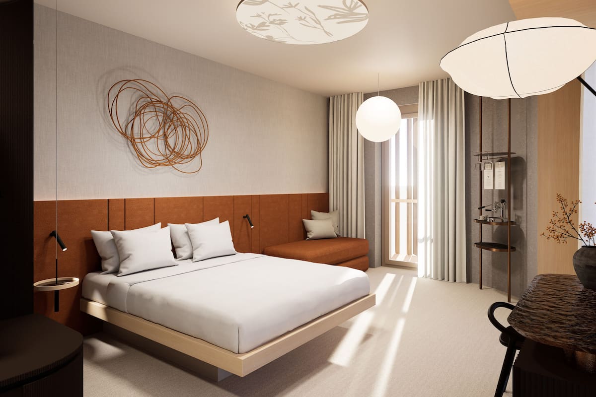 A modern hotel room with a bed, bedside table, lamp, and a view of the outdoors.