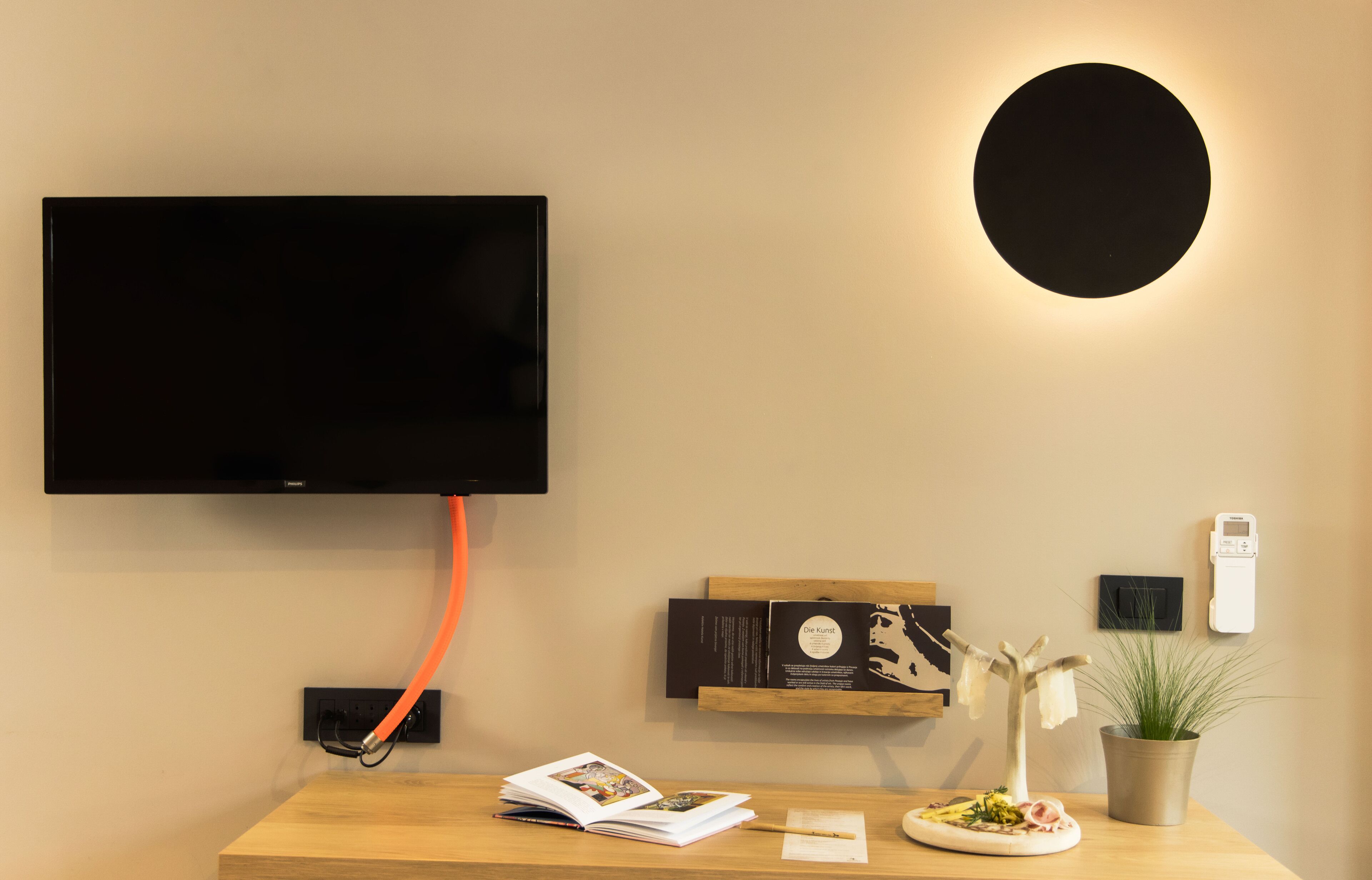Quarto moderno com televisão de tela plana na parede, mesa de madeira com uma revista, uma planta e uma pequena travessa de comida.