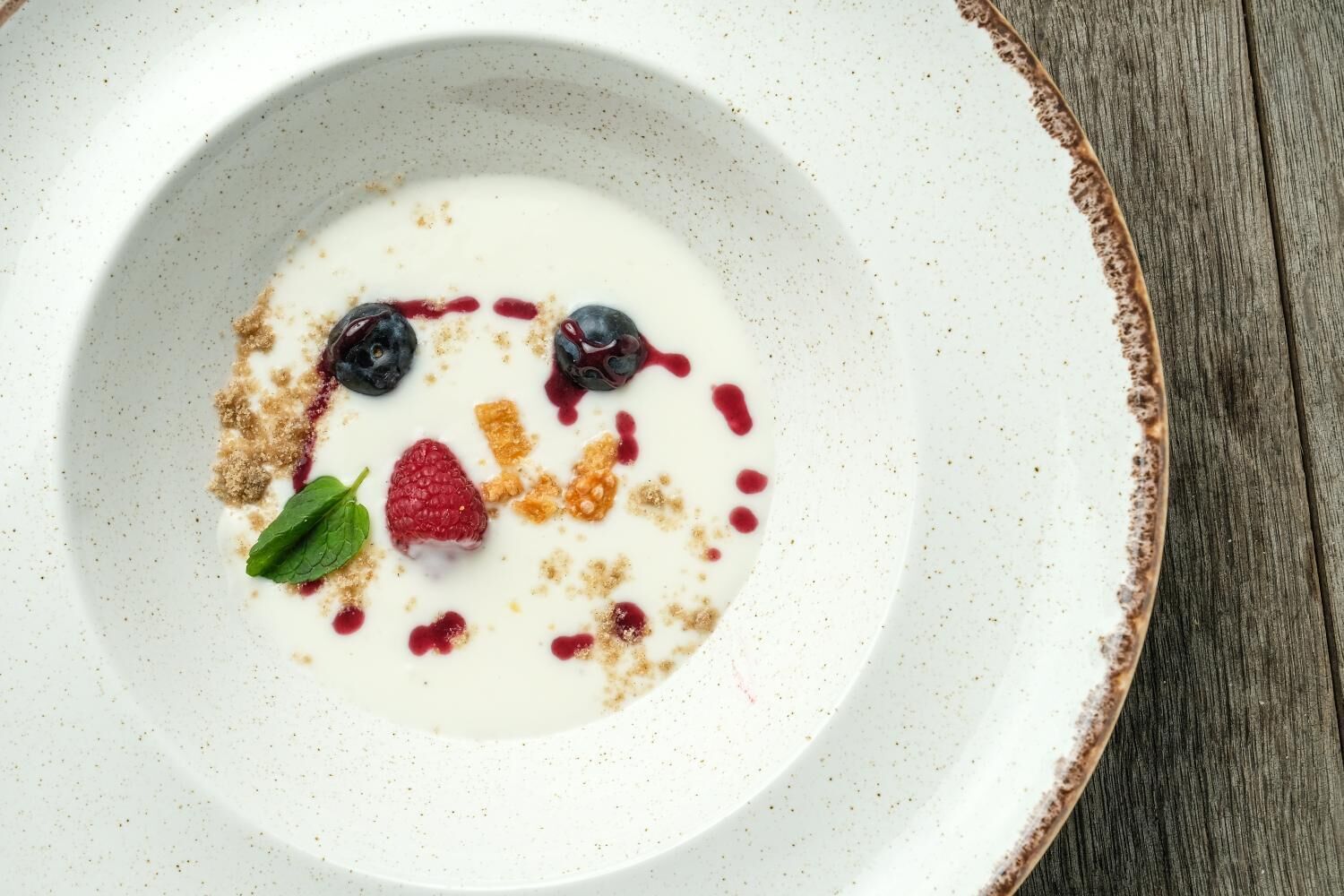 A white plate with a creamy substance, blueberries, raspberries, and a mint leaf.