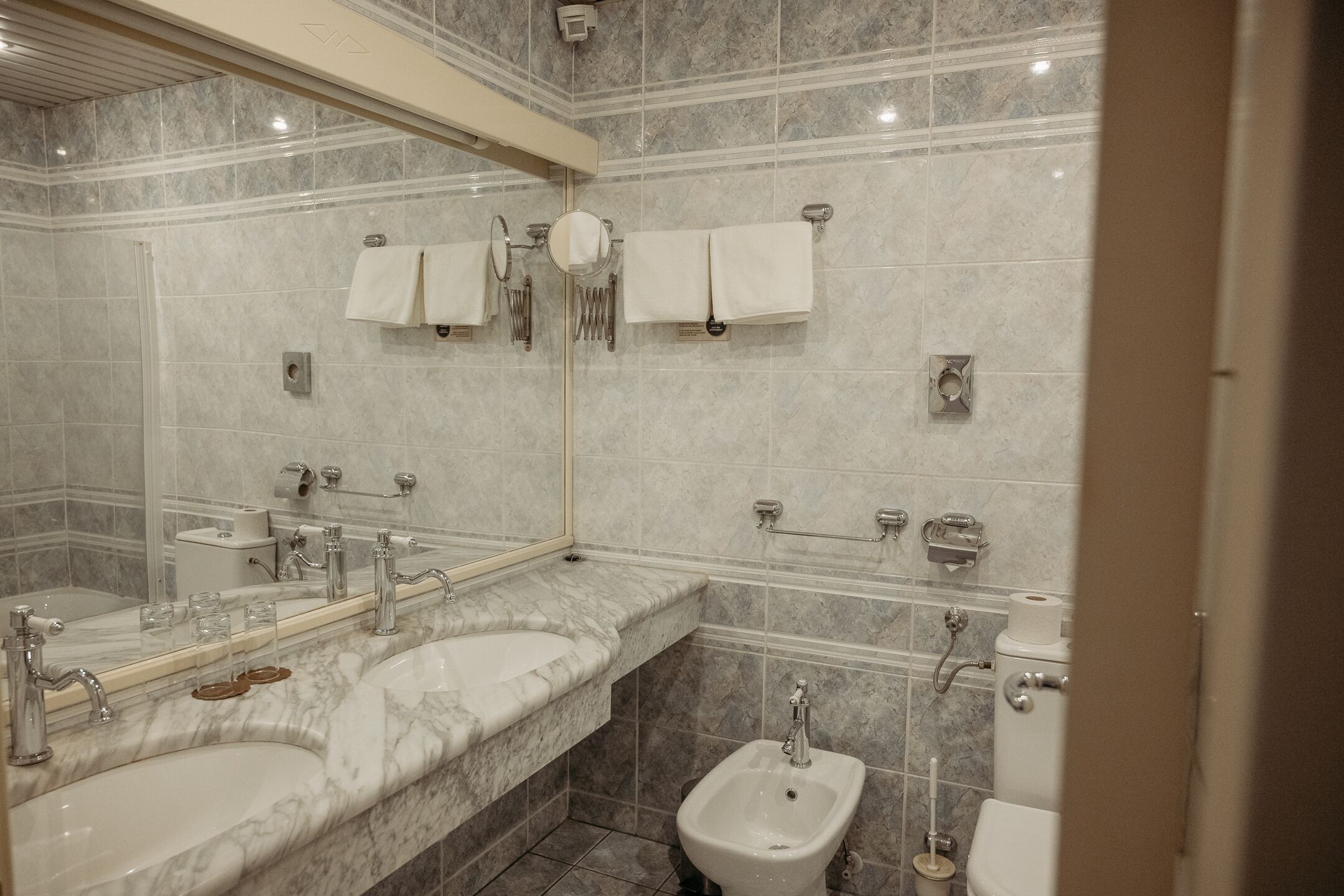 Un baño con dos lavamanos, un bidé, un inodoro y un espejo grande.