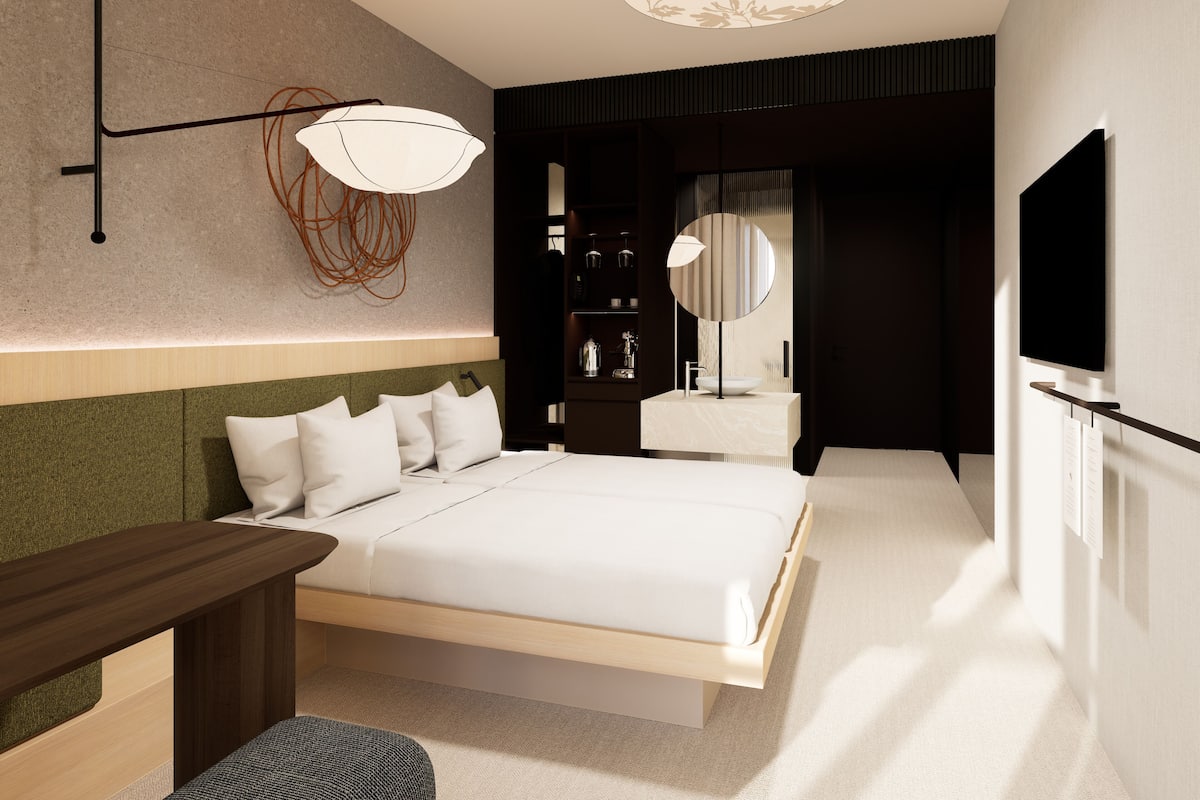 A modern hotel room with a bed, bedside table, lamp, and a large mirror.