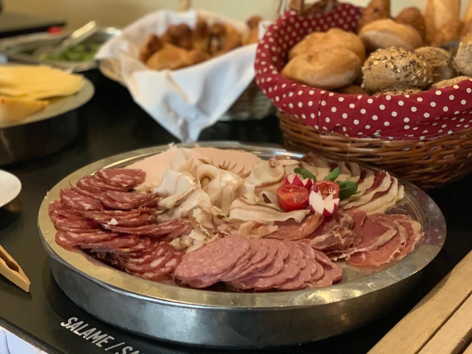 A platter of assorted meats and cheeses, a basket of bread, and a bowl of salad on a table.