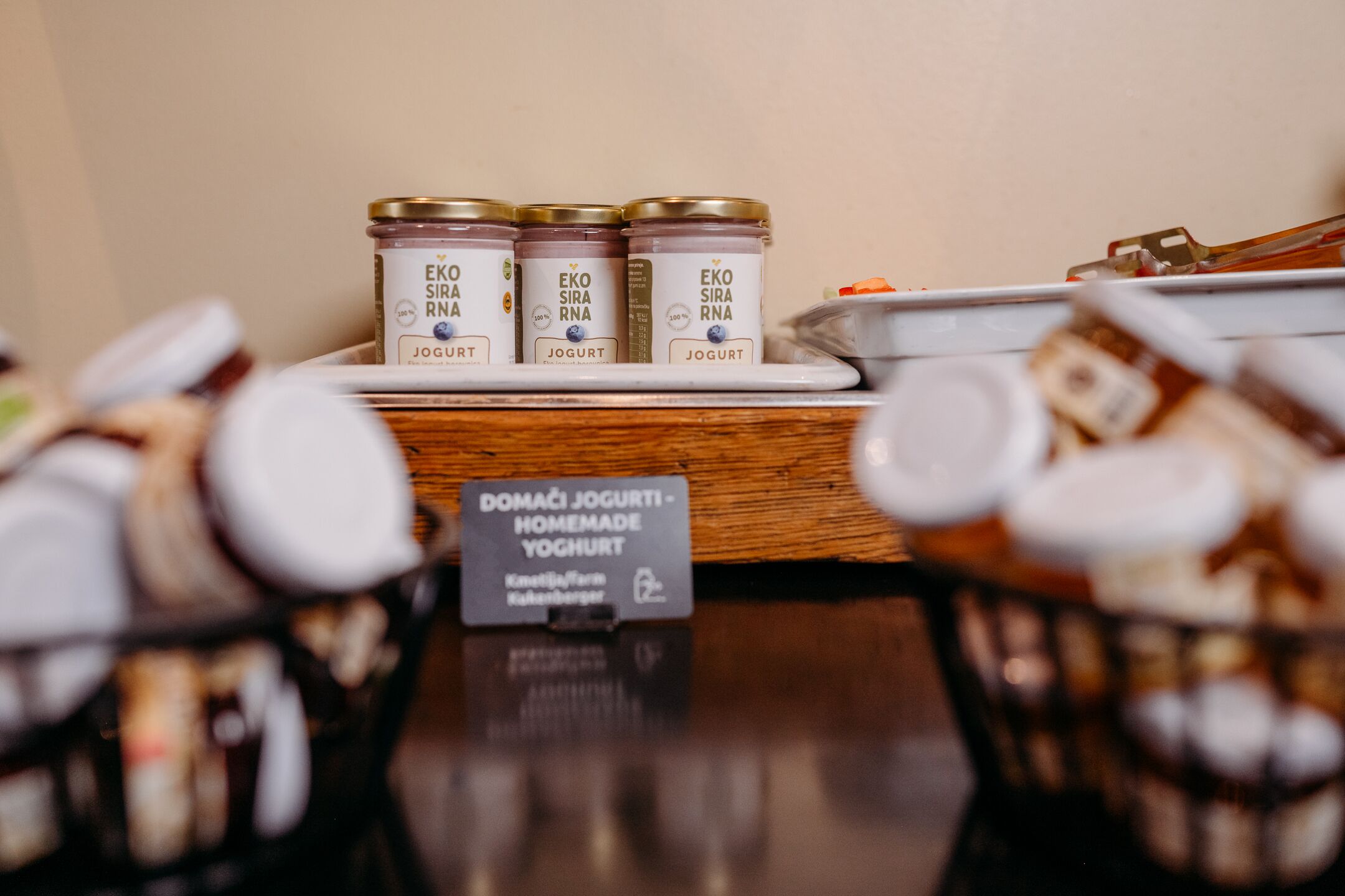 Three jars of EKOS SIRNA yogurt on a wooden surface.