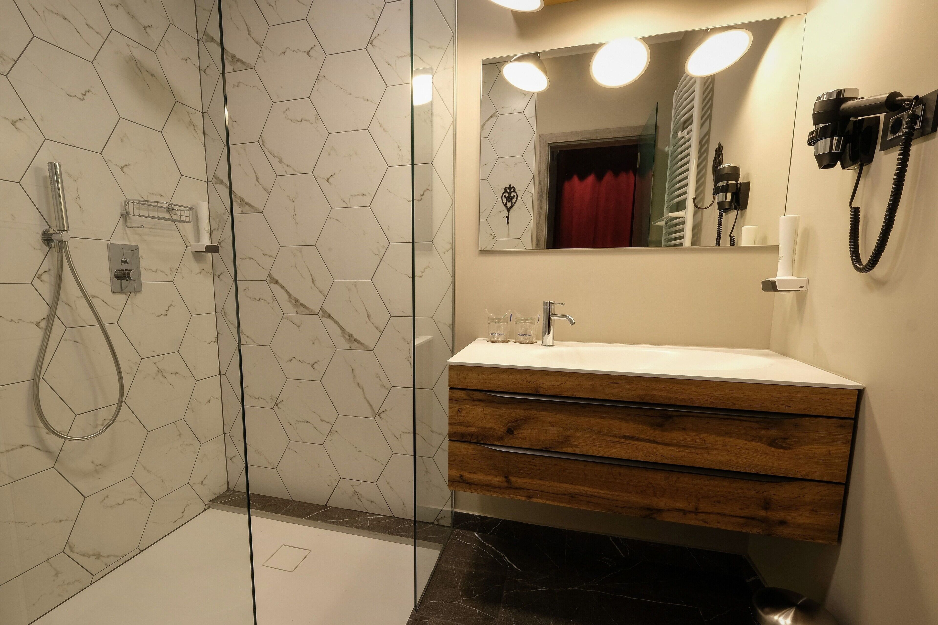 Un baño moderno con ducha de vidrio, tocador de madera con lavamanos blanco e iluminación integrada en el espejo.