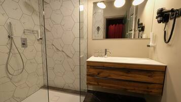Un baño moderno con ducha de vidrio, tocador de madera con lavamanos blanco e iluminación integrada en el espejo.