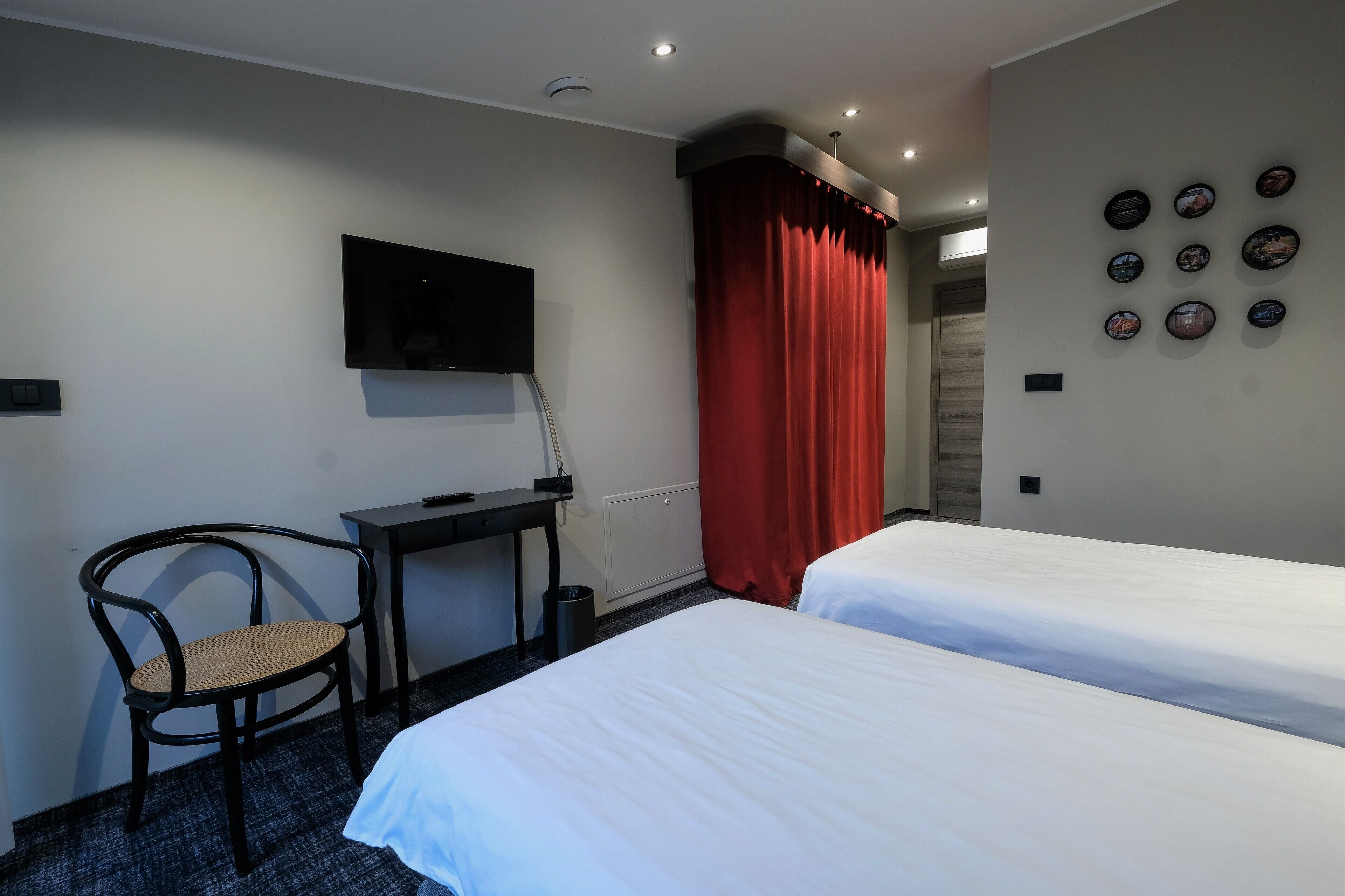 A hotel room with two beds, a desk with a chair, a TV mounted on the wall, and a red curtain.