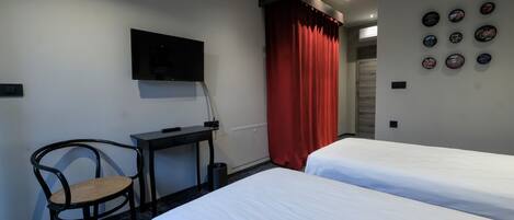 A hotel room with two beds, a desk with a chair, a TV mounted on the wall, and a red curtain.