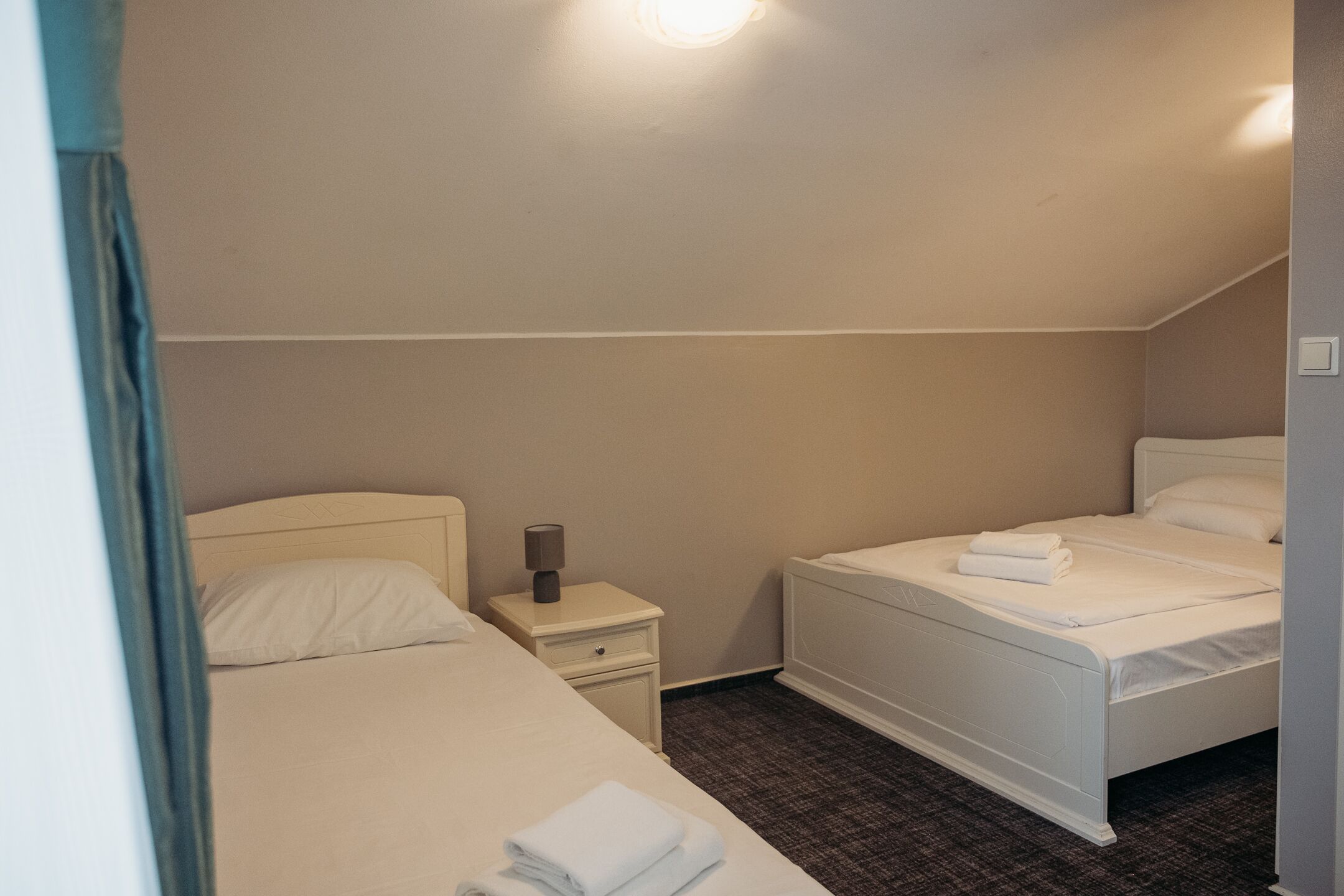 Una habitación de hotel con dos camas, una mesita de noche con lámpara y suelo cubierto de alfombra.