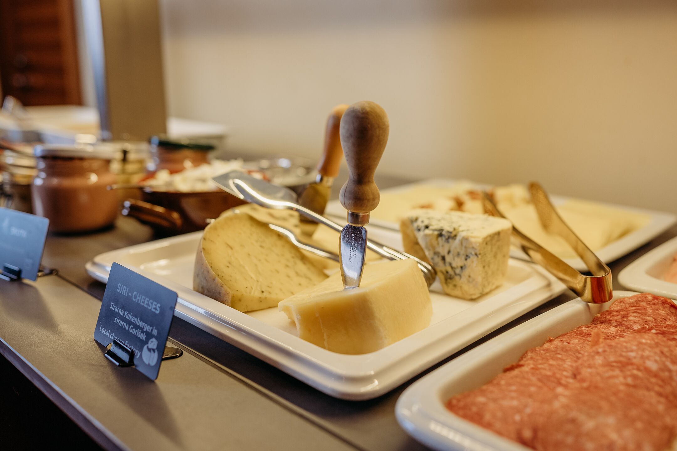 A cheese and meat display with a sign indicating 'Siri - Cheeses' and 'Strame Kukenberger in Siri Chora'.