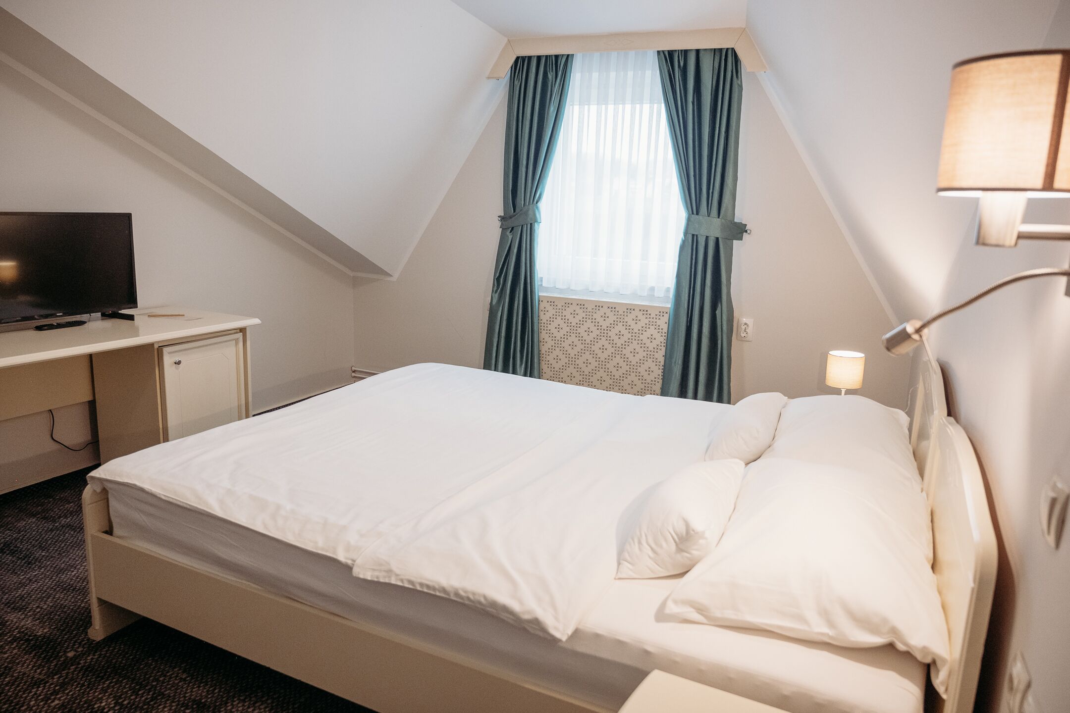 A neatly arranged hotel room with a bed, a desk, a television, and a window with curtains.