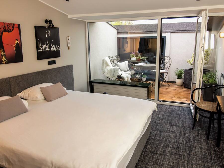Een hotelkamer met een groot bed, een bureau met stoel, een kleine tafel met stoel en een glazen schuifdeur naar een terras.