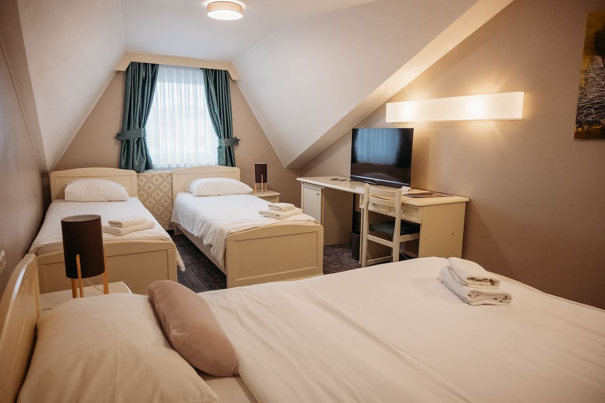 A hotel room with two single beds, a desk with a flat-screen TV, and a large window with curtains.