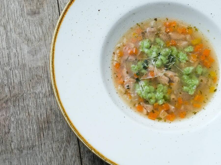 Un bol de sopa amb verdures i herbes sobre una taula de fusta.