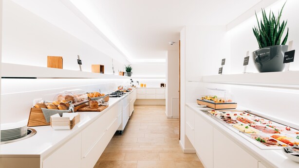 Una cocina moderna con una encimera larga que exhibe diversos alimentos y una vitrina de vidrio con pasteles.